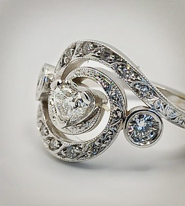 Foto principlae di un anello in oro bianco con diamante centrale a cuore e diamanti sula gambo a spirale