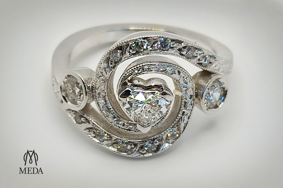Foto principlae di un anello in oro bianco con diamante centrale a cuore e diamanti sula gambo a spirale